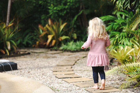 Little girl walking barefoot along tropical garden path