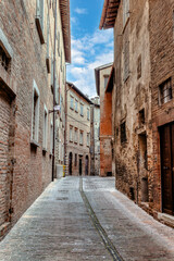 Fototapeta premium A narrow street in Urbino, a medieval town in Italy, where historic buildings with rustic stone facades tower on either side, creating a serene atmosphere.