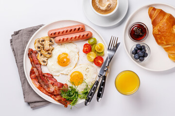 A classic breakfast plate featuring sunny-side-up eggs, crispy bacon, sausages, and fresh tomatoes