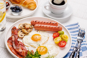 A classic breakfast plate featuring sunny-side-up eggs, crispy bacon, sausages, and fresh tomatoes