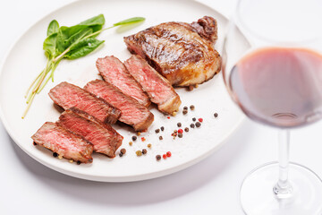 A perfectly cooked sliced striploin steak with a juicy, tender texture, served alongside a glass of rich red wine