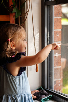 Little girl indoors looking out front window of home