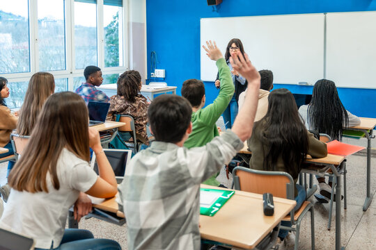 High school students raising hands in classroom during lesson