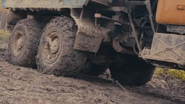 A heavy-duty truck attempts to maneuver through thick mud in a rural area. The tires are deeply buried in the mire, showcasing the difficulties of off-roading after rainfall.