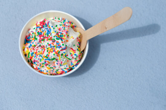 Vanilla soft serve icecream with colourful sprinkles in tub with wooden spoon