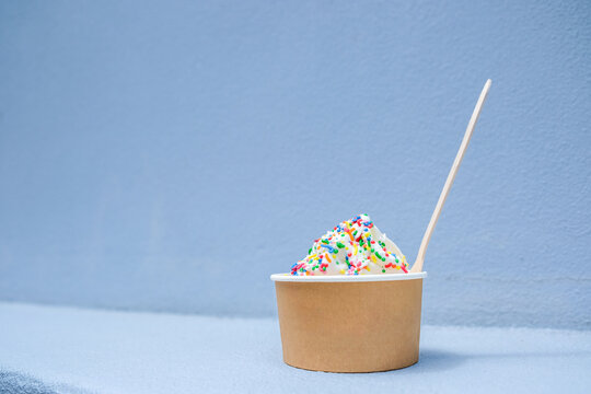 Vanilla soft serve icecream with colourful sprinkles in tub with wooden spoon