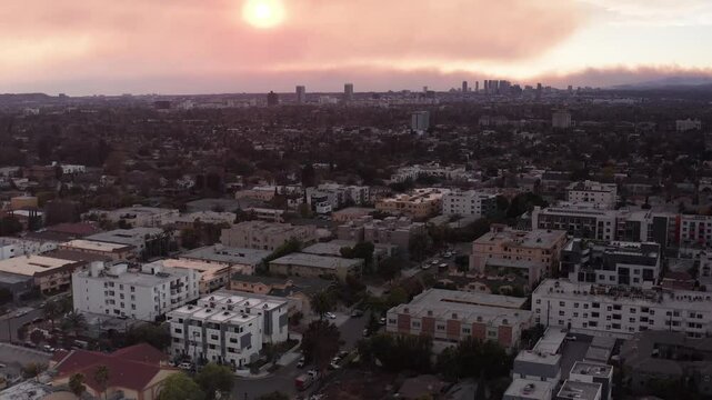 Low aerial shot flying over Melrose Hill with smoke from the Palisades Fire in the horizon at sunset in Hollywood, California. 4K