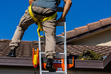 Tradie climbing on roof of house in safety harness to secure rope for safety compliance