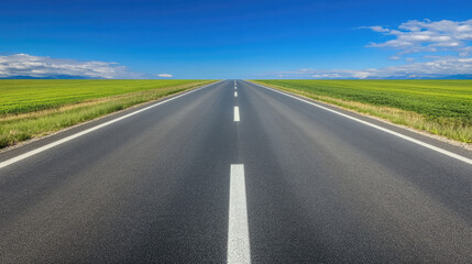 Fototapeta premium Wide road into distance, flanked by green fields and blue sky. High-definition, horizontal composition. Serene beauty.