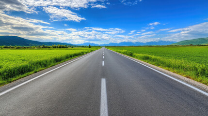 Naklejka premium Wide road into distance, flanked by green fields and blue sky. High-definition, horizontal composition. Serene beauty.