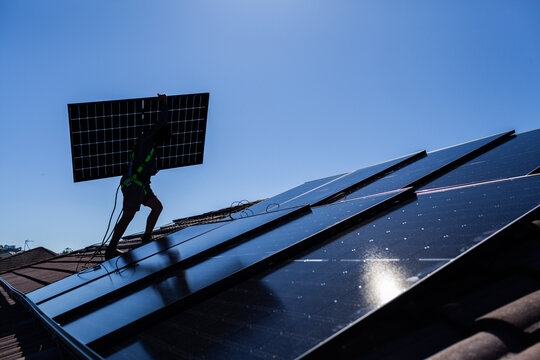 bifacial solar panels being carried on rooftop during solar system installation by electrician