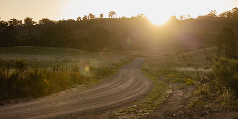 Tranquil rural road through serene sunset landscape with warm hues over grassy fields
