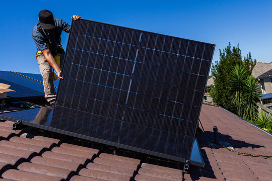 Aussie tradie guy installing solar panels on hot sunlit roof or Australian home