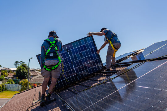Tradesman electrician and apprentice installing solar panel system on rooftop in Australia