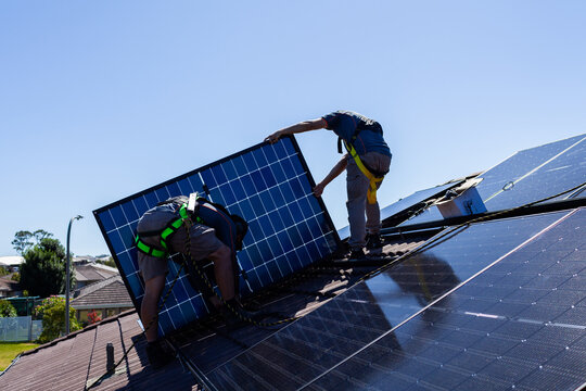 Tradesman electrician and apprentice installing solar panel system on rooftop in Australia