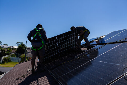 Tradesman electrician and apprentice installing solar panel system on rooftop in Australia