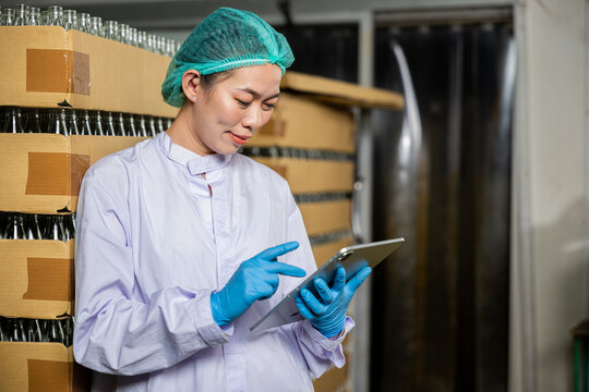 A dedicated QC woman at beverage factory uses a digital tablet to inspect items on the conveyor belt. Her role encompasses quality control while examining the bottling line for liquid manufacturing.