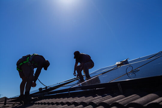 Tradesman electrician and apprentice installing solar panel system on rooftop in Australia