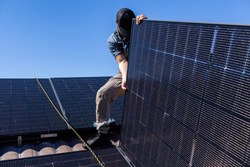 Electrician tradie working on solar panel installation laying panels onto roof of Australian home