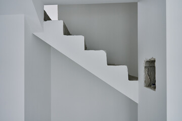 Unfinished concrete staircase in modern minimalist interior. New apartment with raw construction elements and white walls. Building under repair