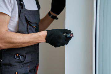 Construction worker in gloves uses laser distance measurer to inspect wall. Builder using digital tool for precision measurement during repair work. Construction and renovation concept