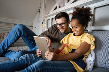 Single father playing with his multiethnic, diverse kid on the bed with digital tablet at home
