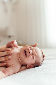 Mother's hand holding crying newborn baby on the bed