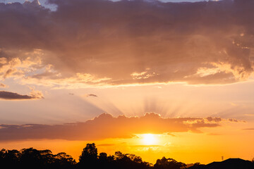 Skyscape of golden rays of sunlight from behind clouds floating in sky at sunrise