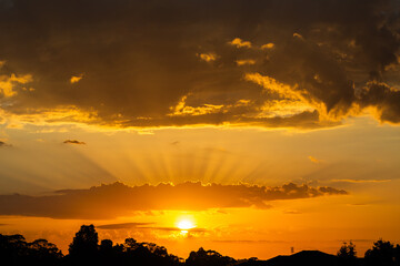Skyscape of sun with golden rays of light from behind clouds at sunrise