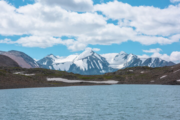 Closeup of ripples on shiny azure water surface of mountain lake against three snowy peaked tops. Nature background of turquoise alpine lake and snow-covered range with few most beautiful pointy peaks
