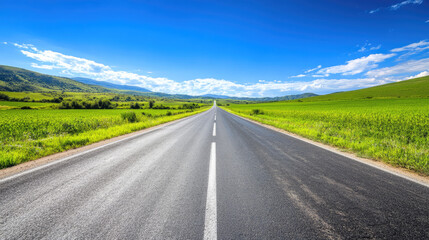 Fototapeta premium Wide road into distance, flanked by green fields and blue sky. High-definition, horizontal composition. Serene beauty.