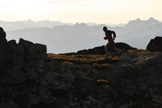 Sunset silhouette of a trail runner on mountain terrain.