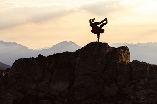 Hispanic man does a parkour handstand on top of rock in mountains