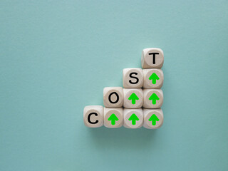 Stacking of cost wording on the top of wooden block cube with up arrow for cost of product and...