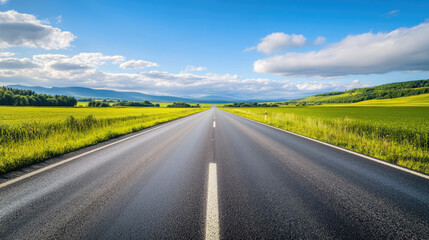 Wide road into distance, flanked by green fields and blue sky. High-definition, horizontal composition. Serene beauty.