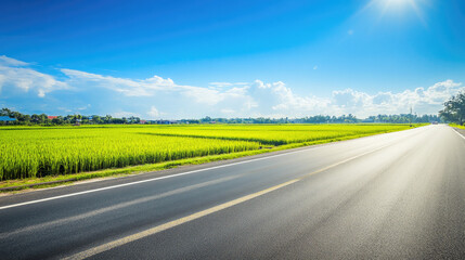 Fototapeta premium Wide road into distance, flanked by green fields and blue sky. High-definition, horizontal composition. Serene beauty.