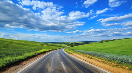 Fototapeta premium Wide road into distance, flanked by green fields and blue sky. High-definition, horizontal composition. Serene beauty.