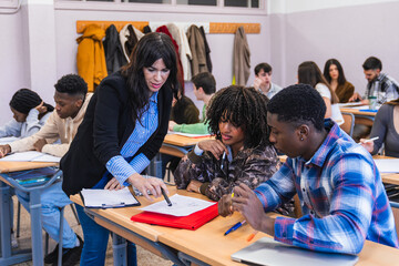 High school teacher helping students studying together in classroom