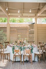 A romantic wedding table setup under a rustic gazebo, featuring a round table with elegant floral decor in soft pink and green tones, gold candlesticks, and vintage green glassware. The 