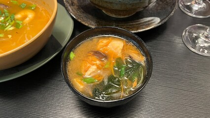 Close-up shot of a steaming bowl of miso soup, a staple of Japanese cuisine. Served in a traditional black lacquer bowl.  Perfect for illustrating healthy eating, Japanese culinary traditions