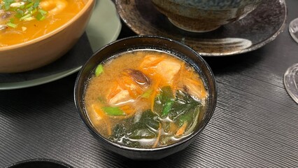 Close-up shot of a steaming bowl of miso soup, a staple of Japanese cuisine. Served in a traditional black lacquer bowl.  Perfect for illustrating healthy eating, Japanese culinary traditions