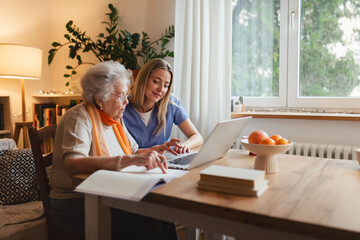Social worker helping elderly lady with managing her finances, teaching her to use online banking...