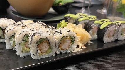 Close-up shot of a platter featuring two types of sushi rolls. The platter rests on a dark rectangular plate. Japanese cuisine, seafood, and healthy eating concept.