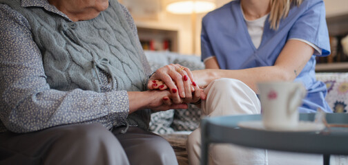 Close up of holding hands of healthcare worker and senior patient.