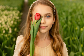 A cute charming girl covered one eye with a tulip. photo session in a greenhouse