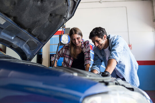 Cheerful man and young woman working together on car repair service and fixing car engine together