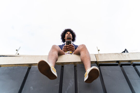 Low angle view of stylish man with cell phone sitting on a wall