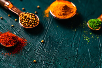 Spices in copper measuring spoons on a malachite textured background. Bright turmeric, paprika, parsley and coriander. View from above. Close-up.