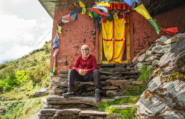 Smiling Backpacker sitting on small sacred Buddhist monastery doorstep decorated multicolored...