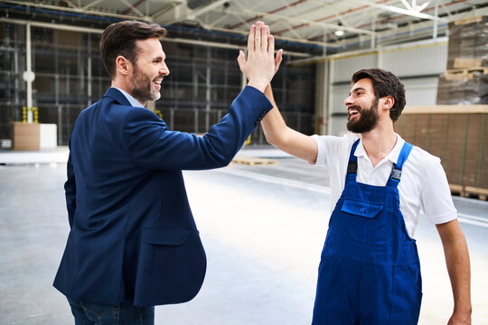 Happy businessman and worker high fiving in a factory
